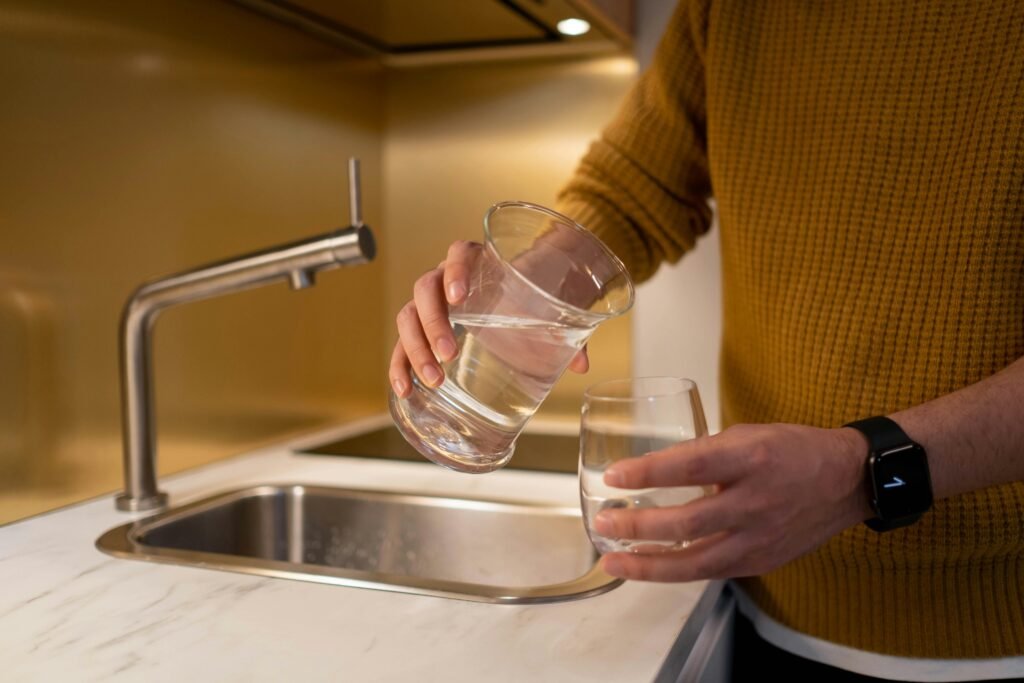 Person pouring water from a pitcher into a glass in a contemporary kitchen setting.